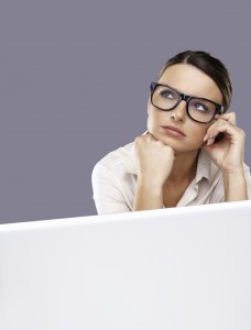 Portrait of a thoughtful business woman wearing spectacle with laptop against grey background