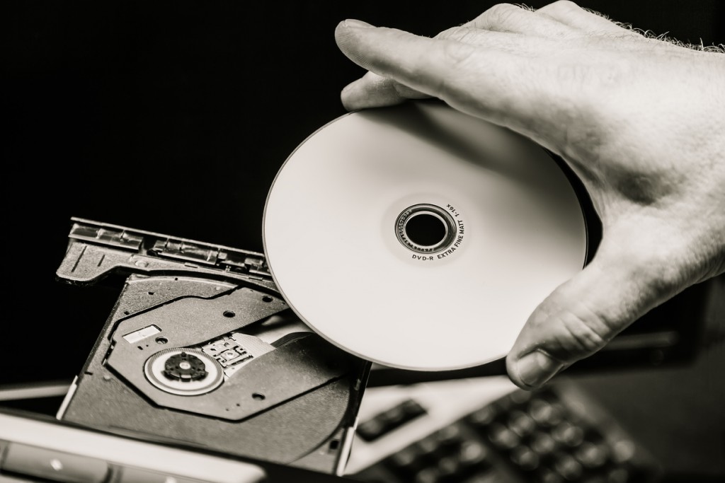 Male hand inserting a DVD into a disk drive. Black and white